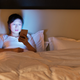 Young woman using a smart phone while in bed at night